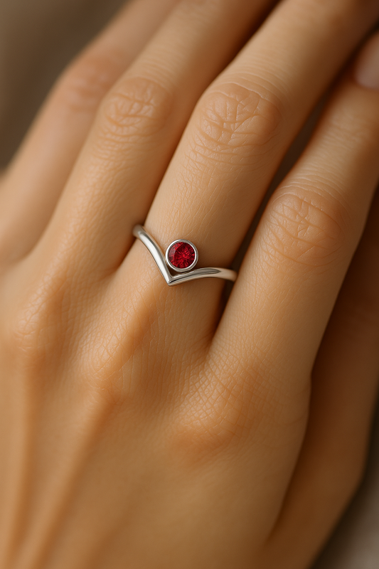 Close-up of a woman’s hand wearing a 14K gold Bezel-Set V Birthstone Ring featuring a natural round ruby, showcasing the elegant split-shank design and polished finish