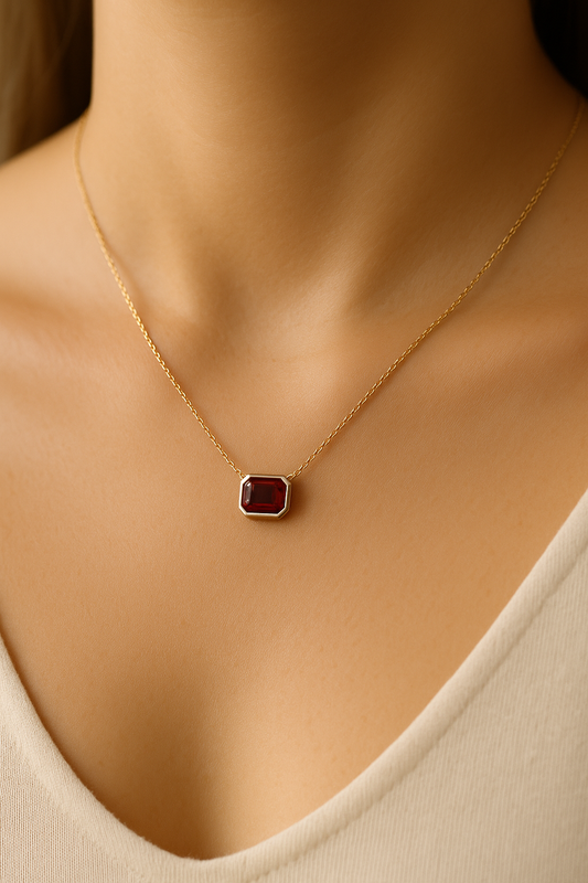 Gold necklace with a red gemstone pendant on a model wearing a beige top.