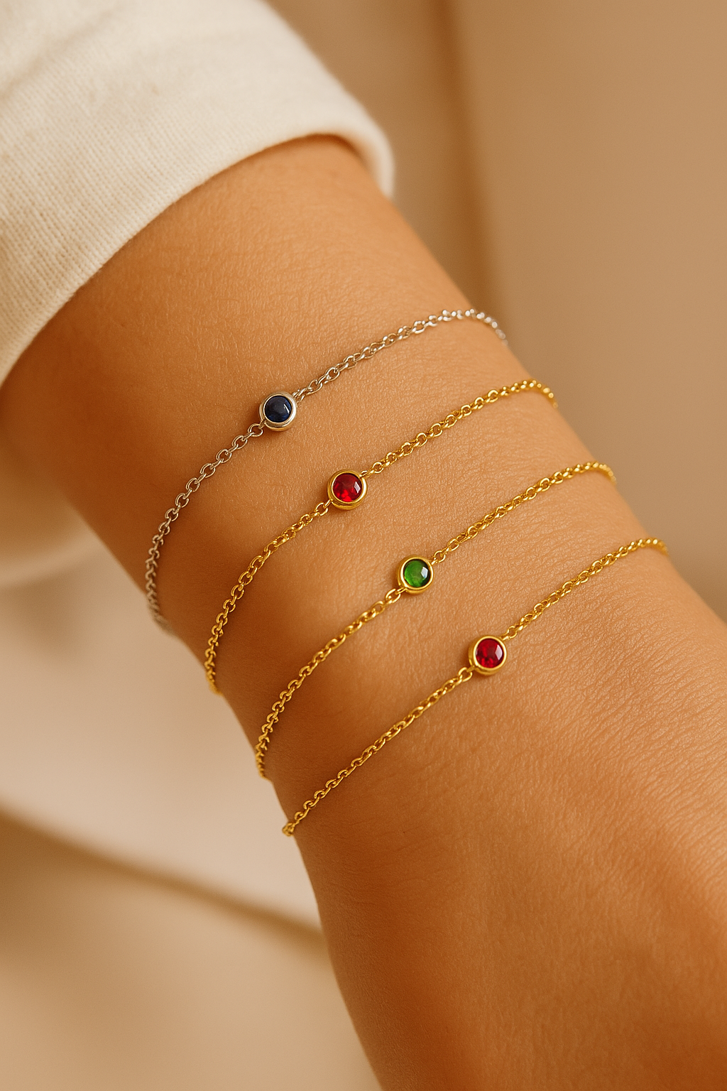 Close-up of a wrist wearing multiple gold bracelets with colored gemstones on a beige background