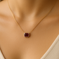 Gold necklace with a red gemstone pendant on a model wearing a beige top.