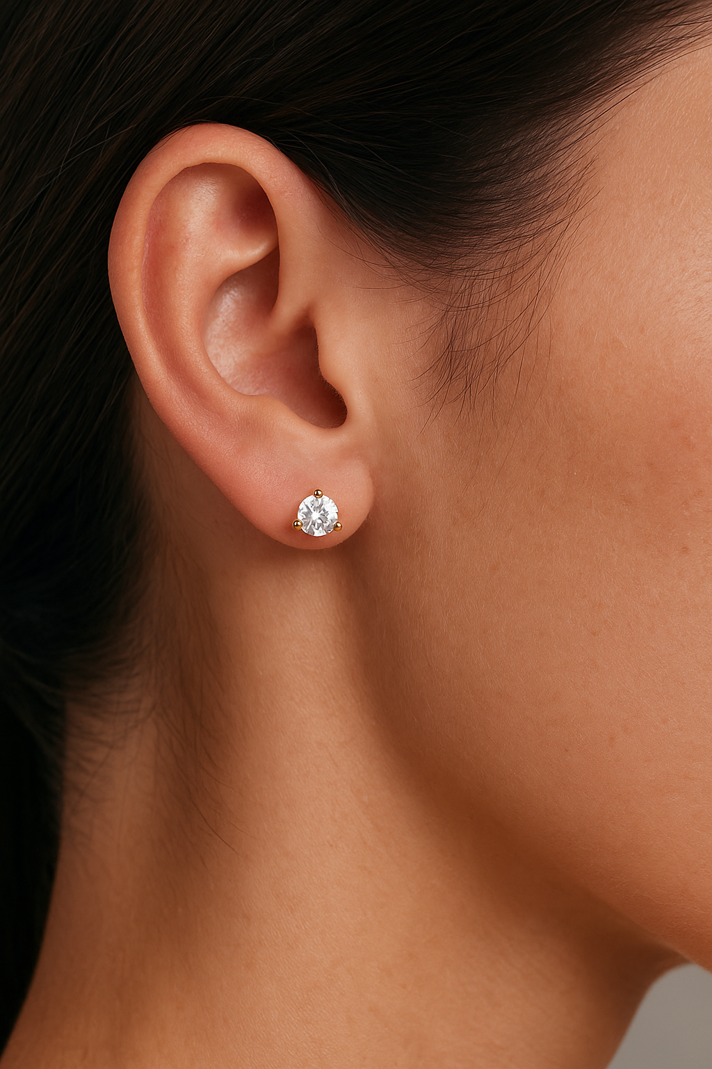 Close-up of a woman's ear wearing a 5 MM round diamond stud earring in a yellow gold 3-prong martini setting (1 CTW total)