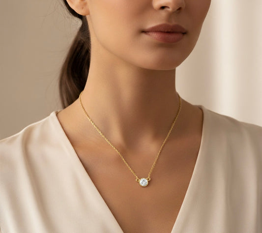 Woman wearing a gold necklace with a diamond pendant against a neutral background